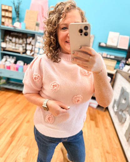 Woman taking a mirror selfie wearing a pink sweater with floral patterns in a store setting.