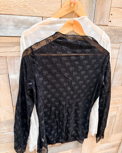 Black lace top with bow pattern on a wooden hanger against a wooden background