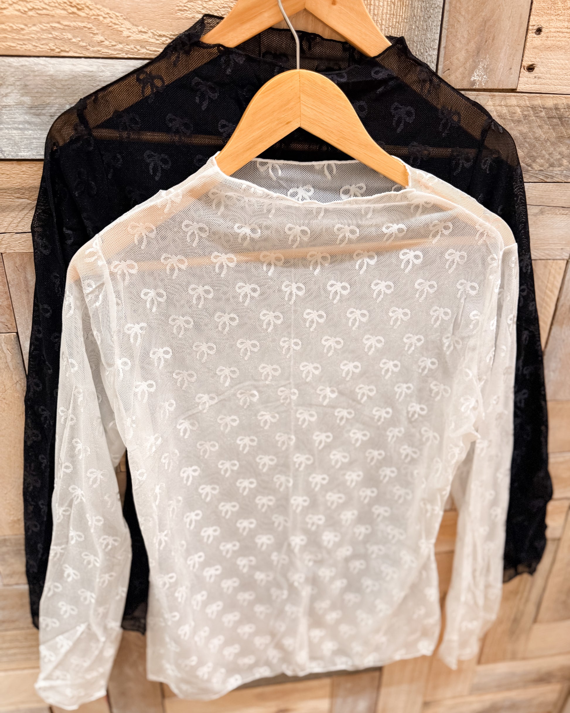Sheer white blouse with bow pattern on a hanger against a wooden background