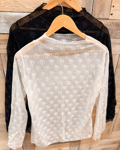Sheer white blouse with bow pattern on a hanger against a wooden background