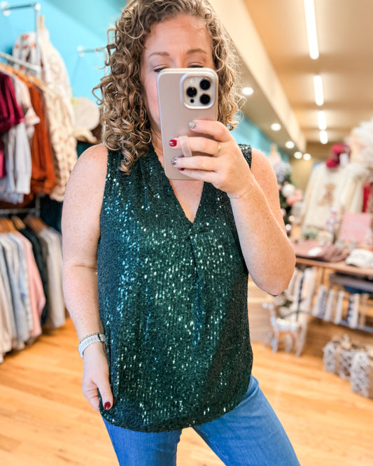 Person taking a mirror selfie wearing a green sequin top in a clothing store.