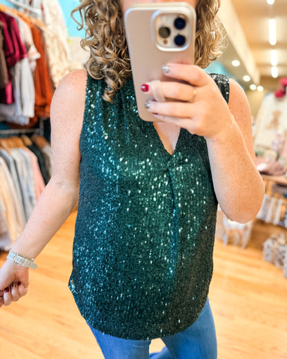 Person wearing a green sequin top taking a mirror selfie in a store.