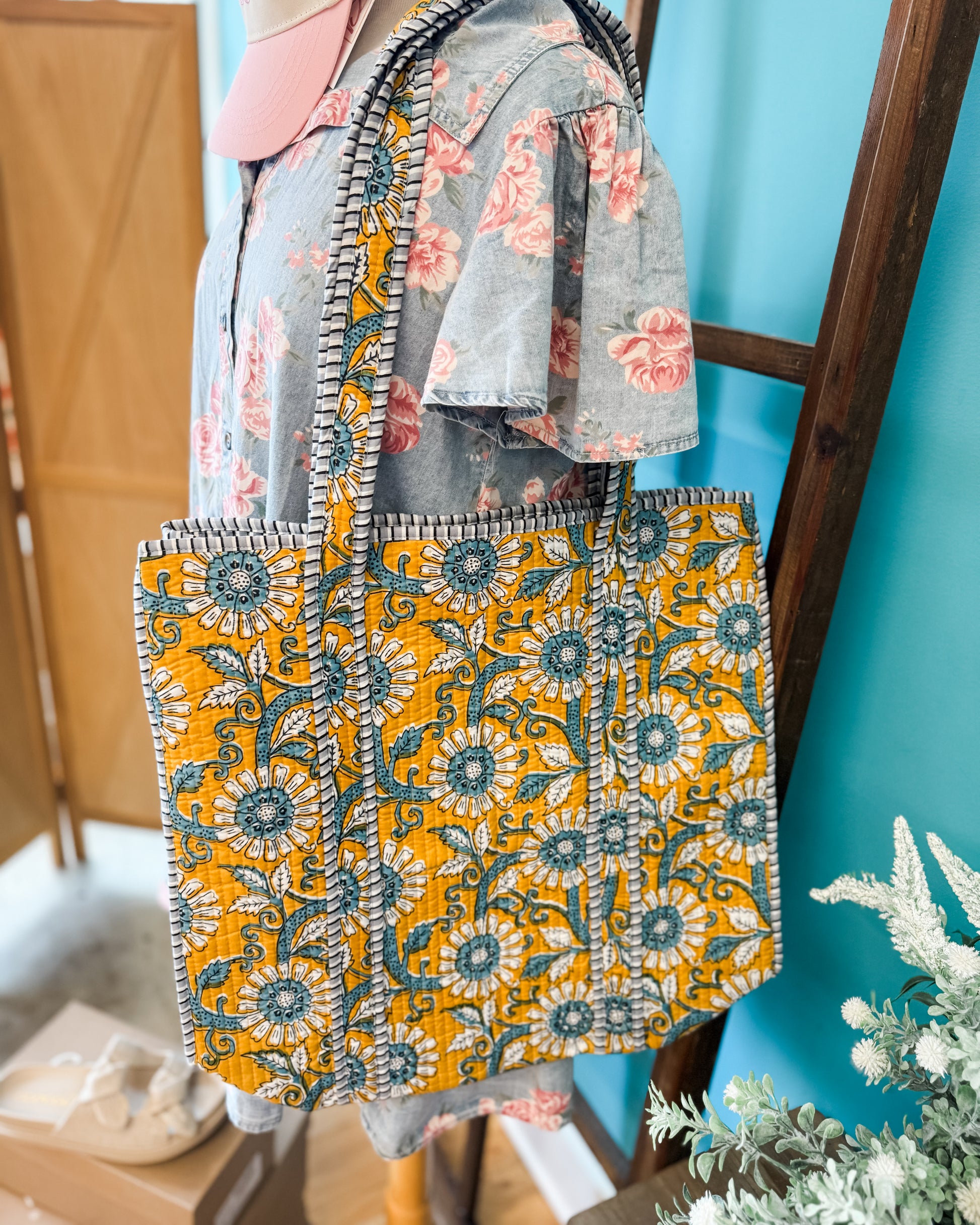 Floral-patterned bag with a yellow and blue design held by a person against a blue wall.