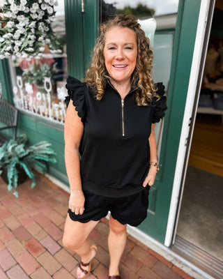 Soft Luxe-Cotton two-piece short set featuring a ruffled half-zip sweatshirt and matching shorts. A comfortable, feminine lounge set perfect for travel, errands, and everyday casual style.