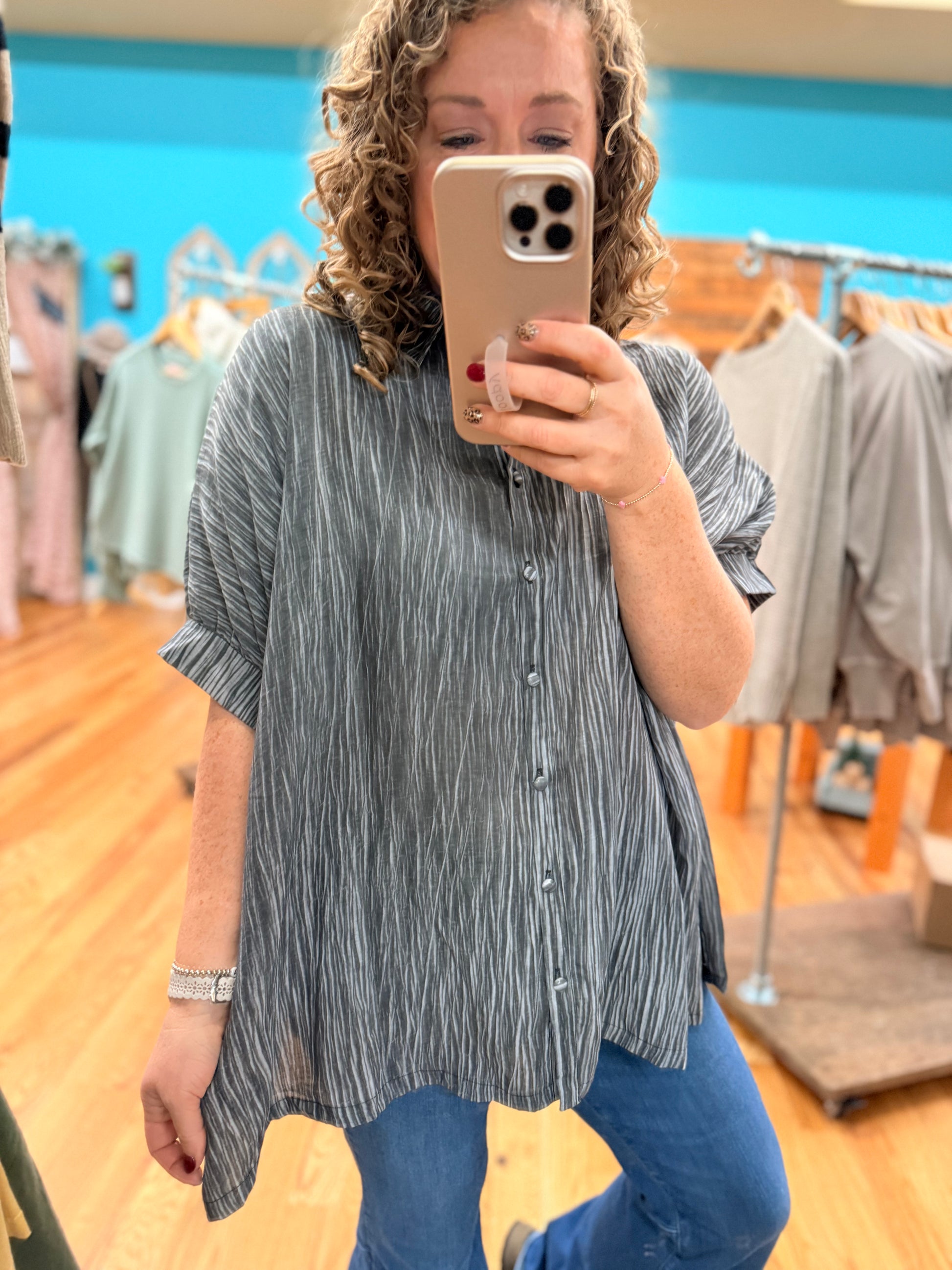 Person taking a mirror selfie wearing a striped shirt and blue jeans in a clothing store.