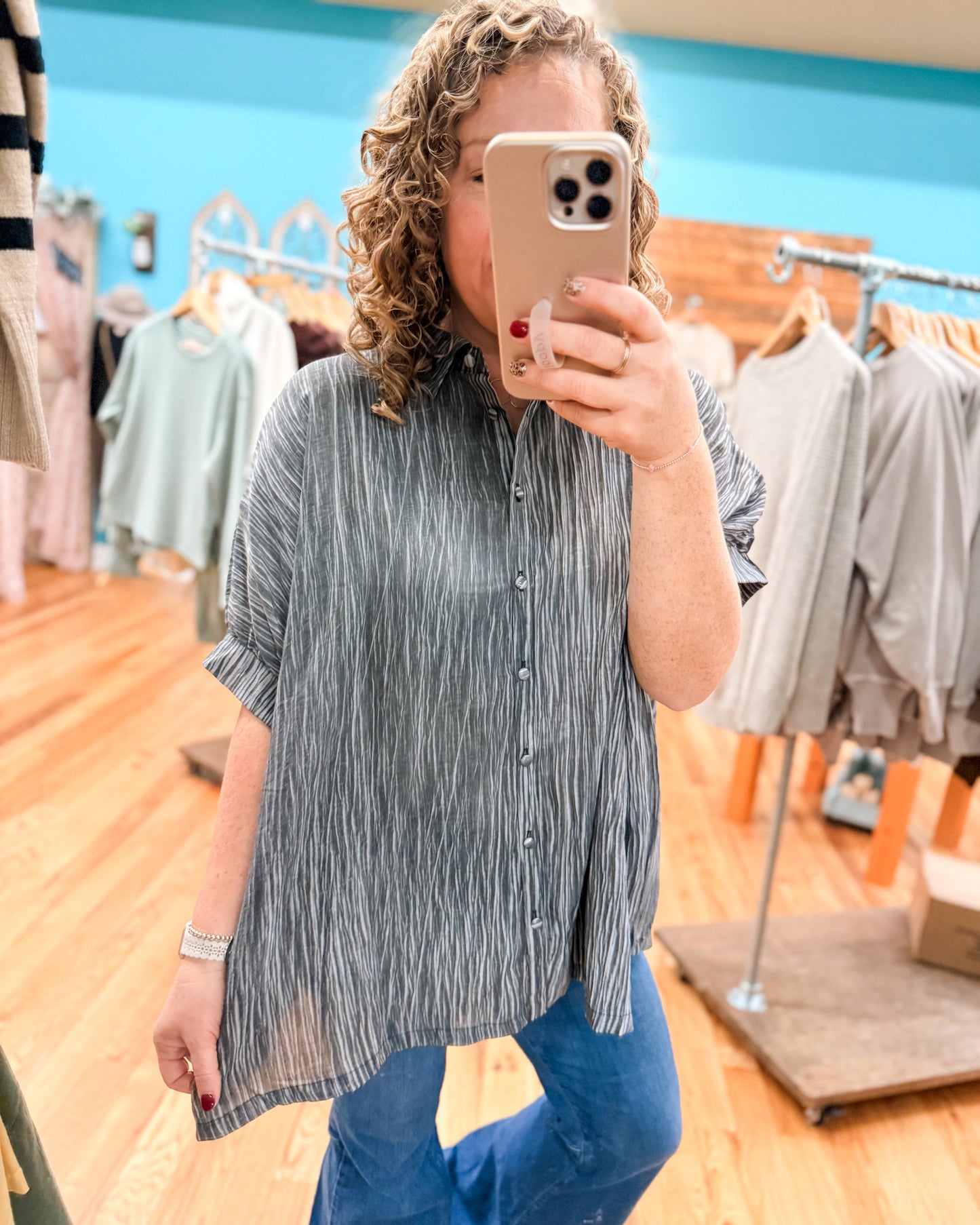 Woman taking a mirror selfie in a clothing store wearing a striped shirt and blue pants.
