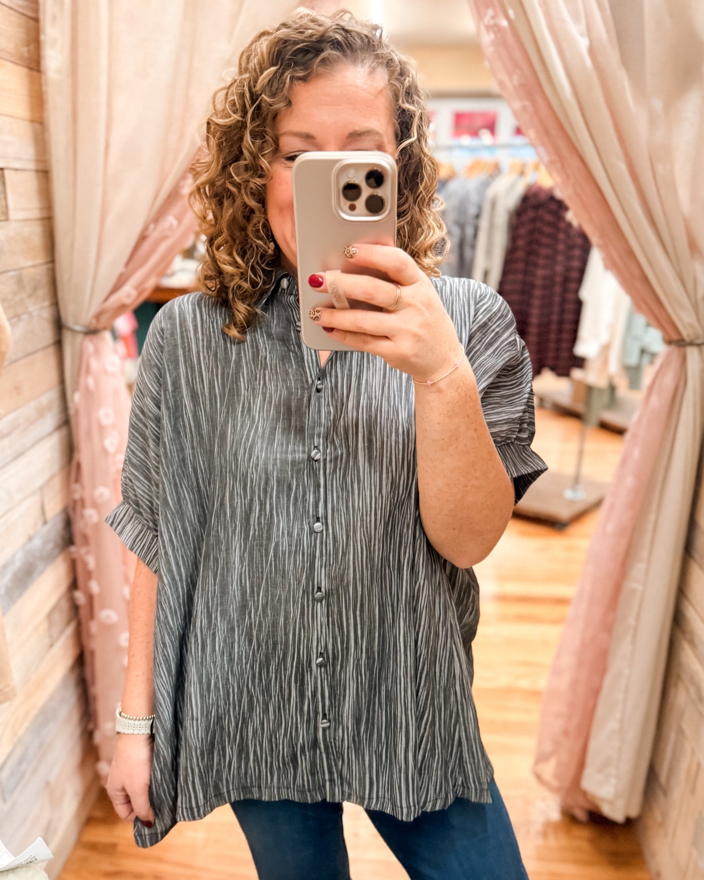Woman taking a mirror selfie wearing a striped shirt in a clothing store.