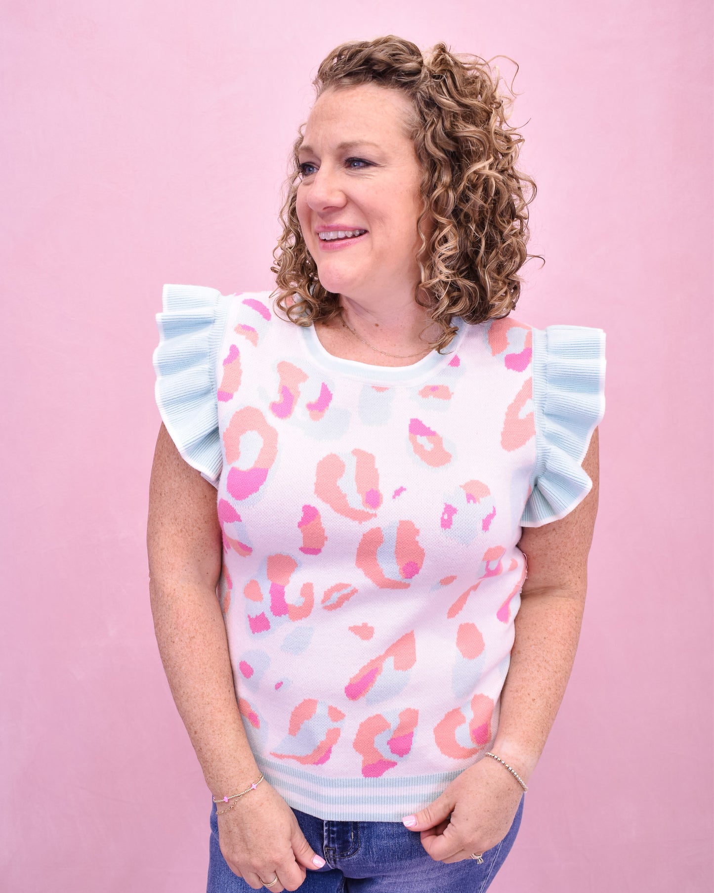 Woman wearing a white top with pink leopard print and ruffled sleeves against a pink background
