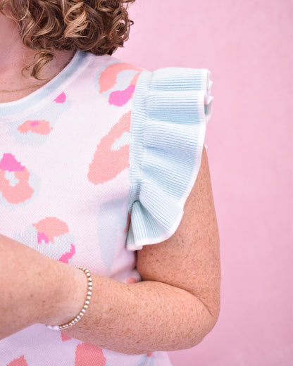Woman wearing a sleeveless top with floral pattern and ruffled sleeves against a pink background