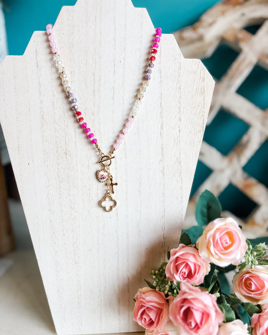A charm necklace with a porcelain heart charm and cross charm on a beaded chain with pink details