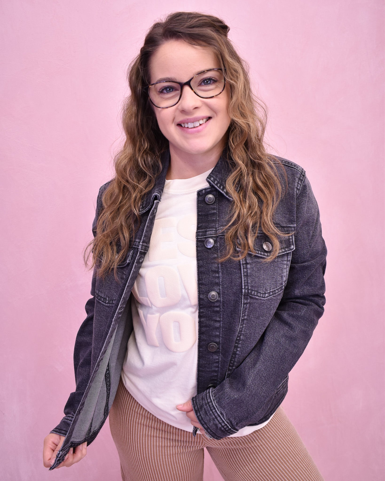 Woman wearing a denim jacket over a white shirt with a pink background