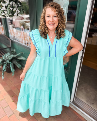 a mint and blue tiered midi dress in a seersucker material with ruffle flutter sleeves and piping details.