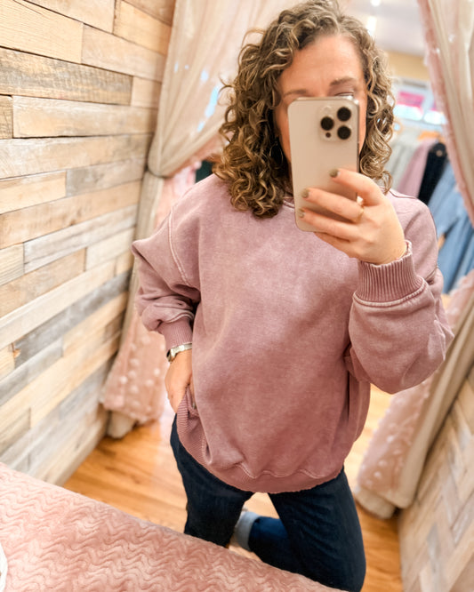 Person wearing a pink sweatshirt taking a mirror selfie in a store.