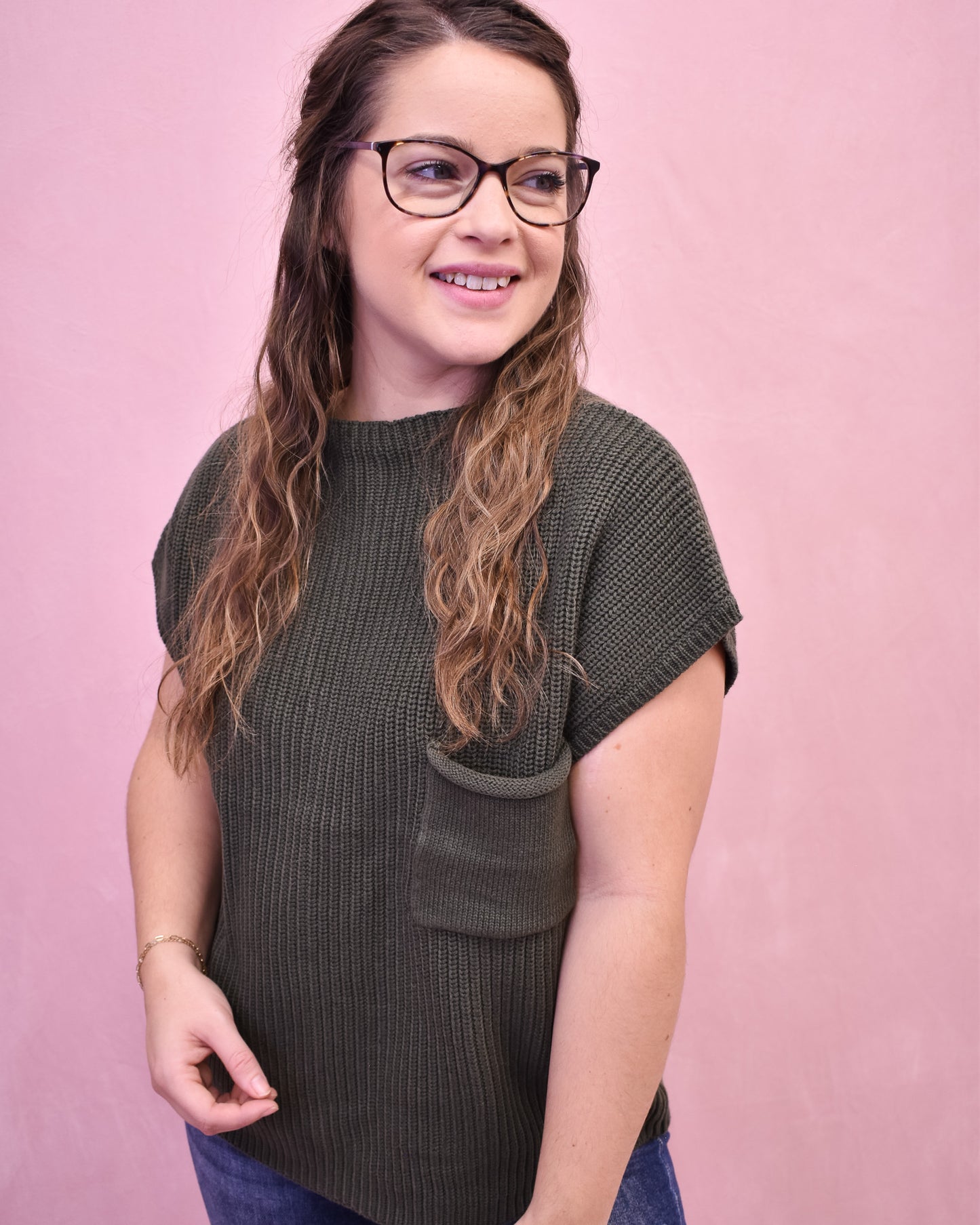 Woman wearing a dark green sleeveless top with a pocket against a pink background