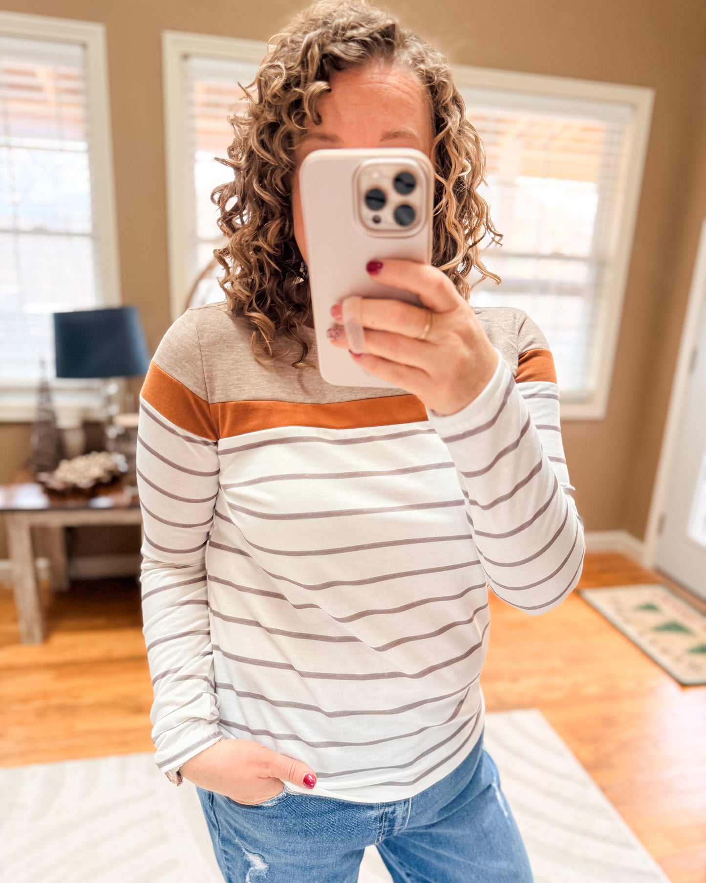 Person taking a mirror selfie wearing a striped sweater and jeans in a home setting.