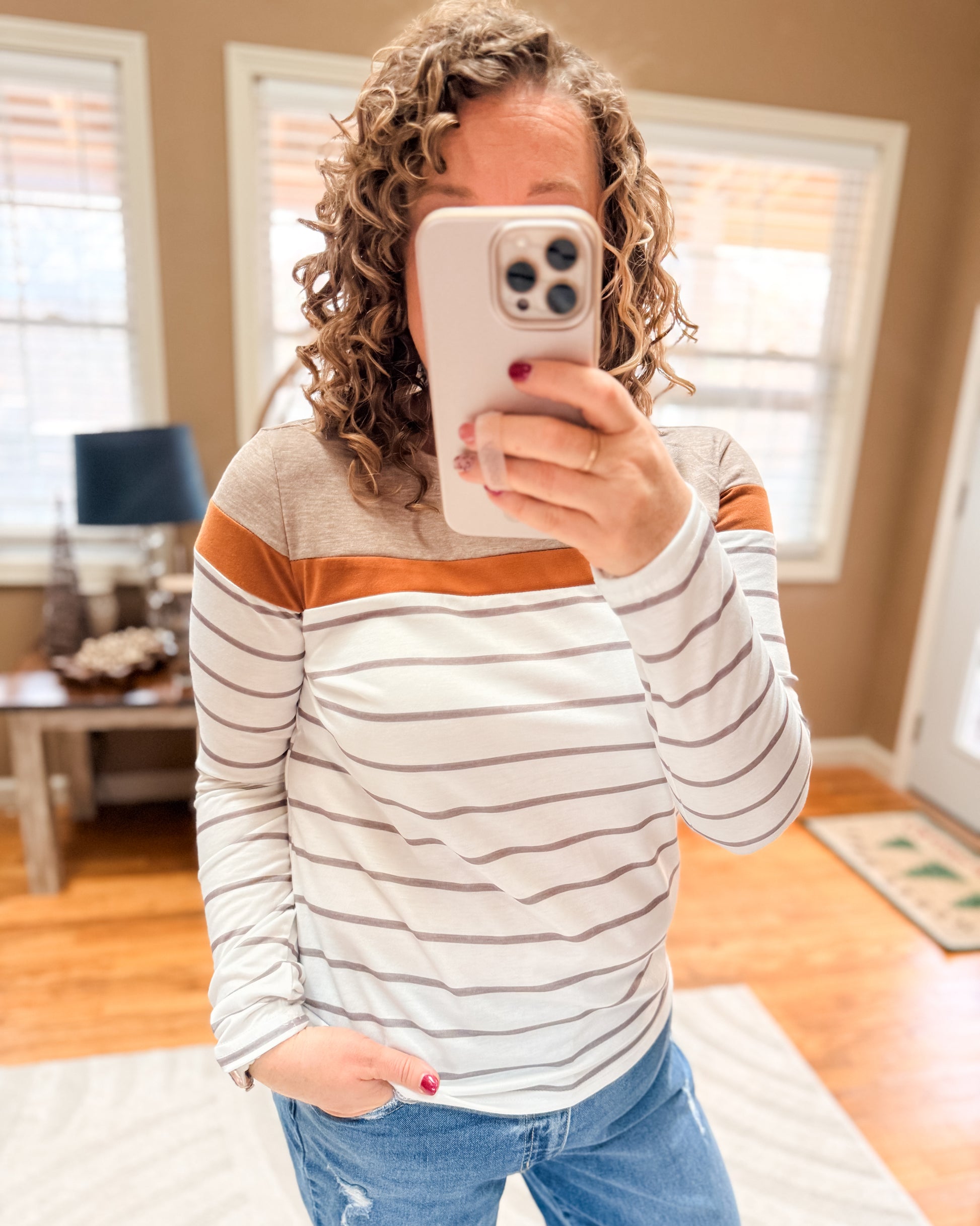 Person taking a mirror selfie wearing a striped sweater and jeans in a home setting.