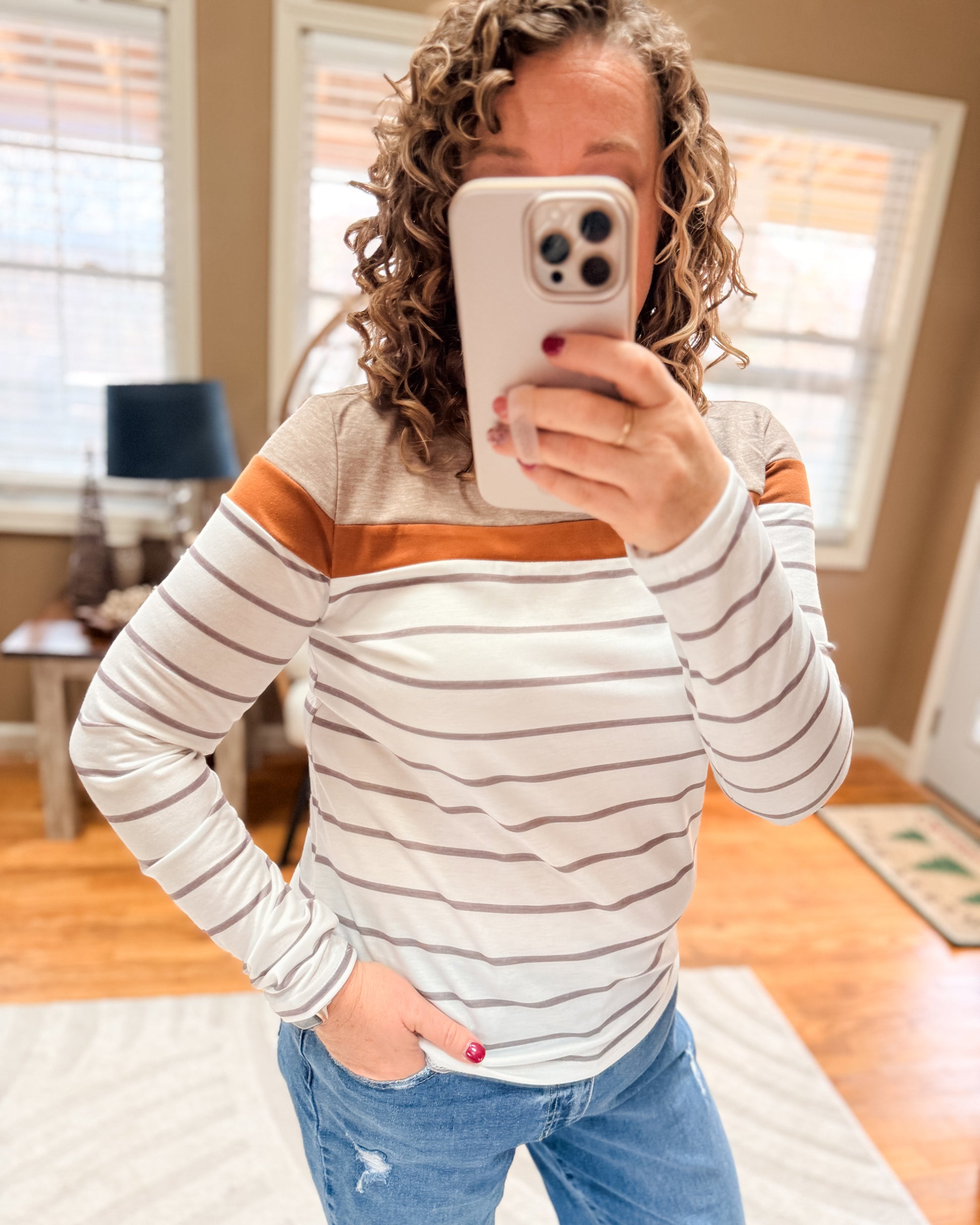 Person wearing a striped long-sleeve top and blue jeans, taking a mirror selfie.