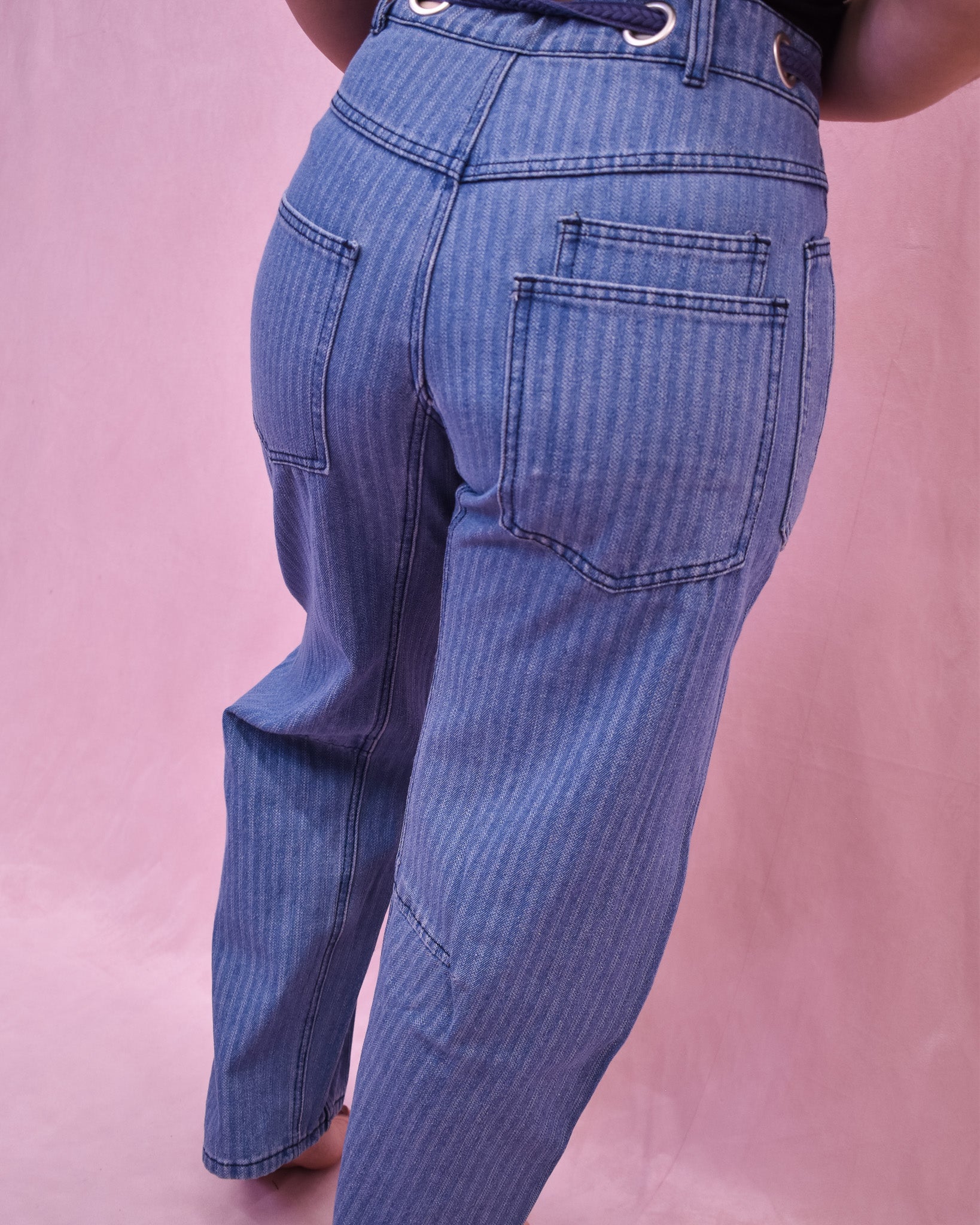 Blue jeans worn by a person on a pink background