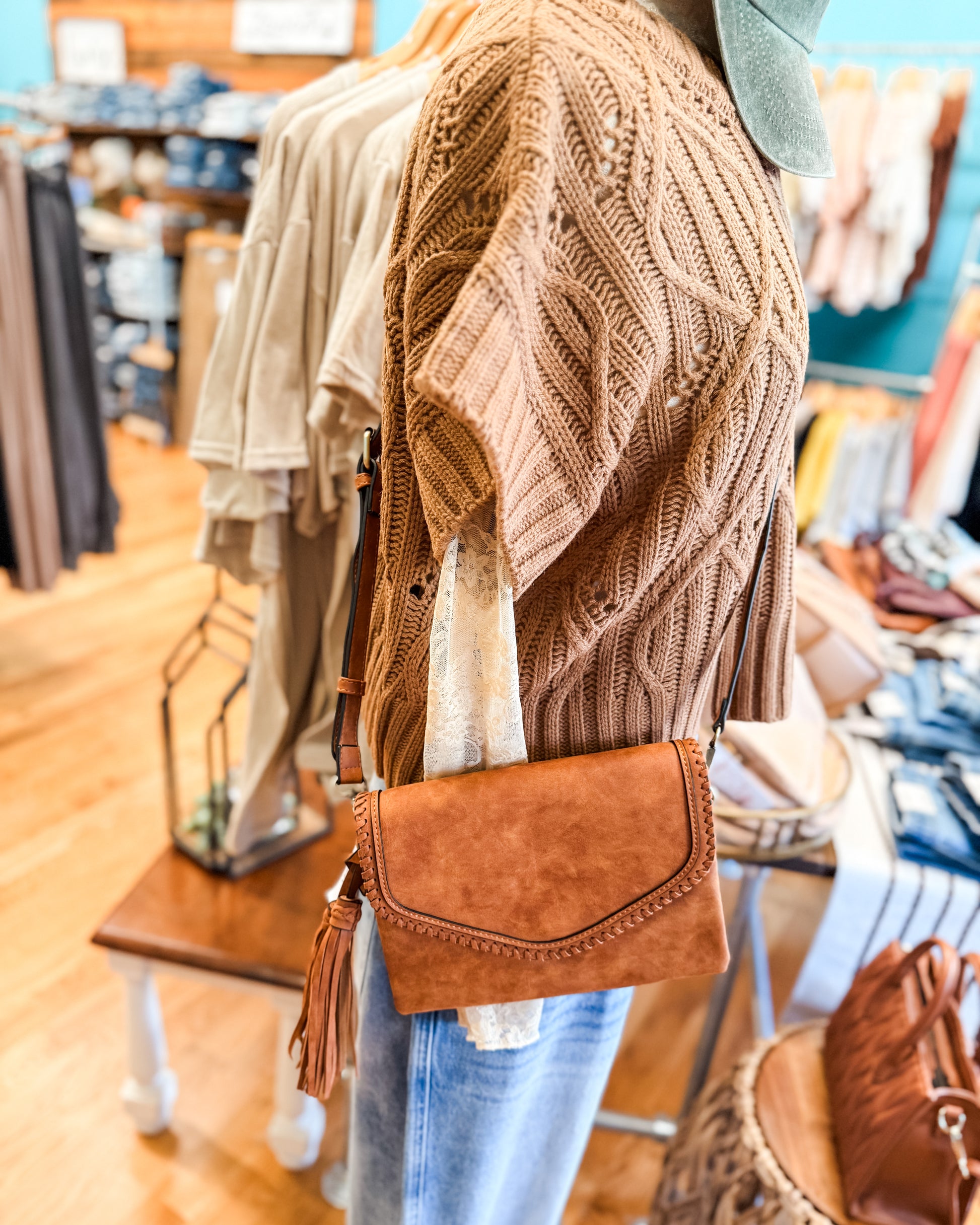 Person wearing a brown knitted cardigan and holding a brown handbag in a store setting.