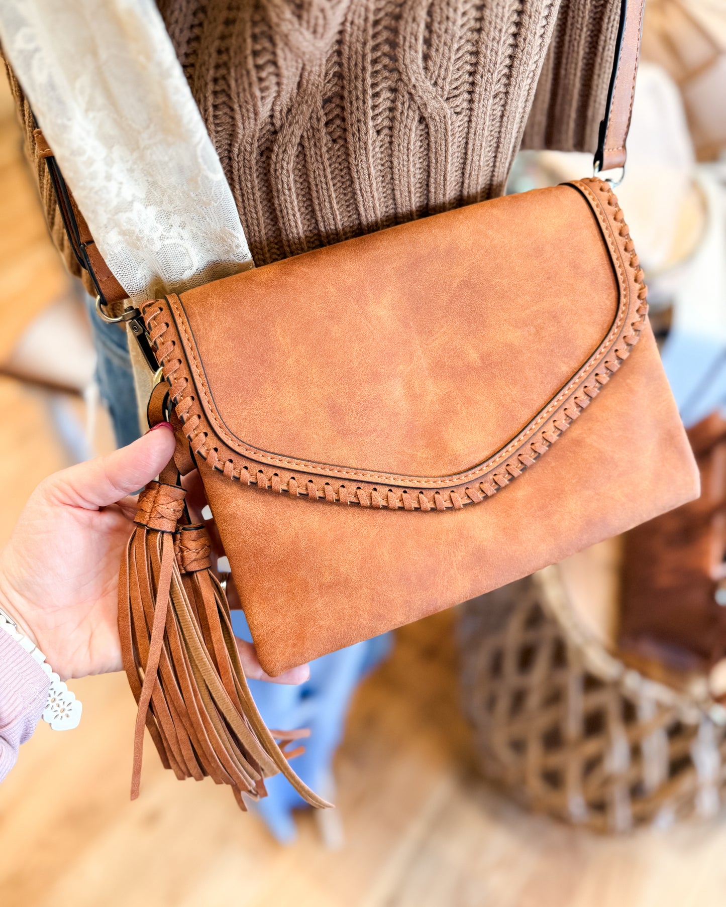 Brown leather clutch with tassel held by a hand, blurred background