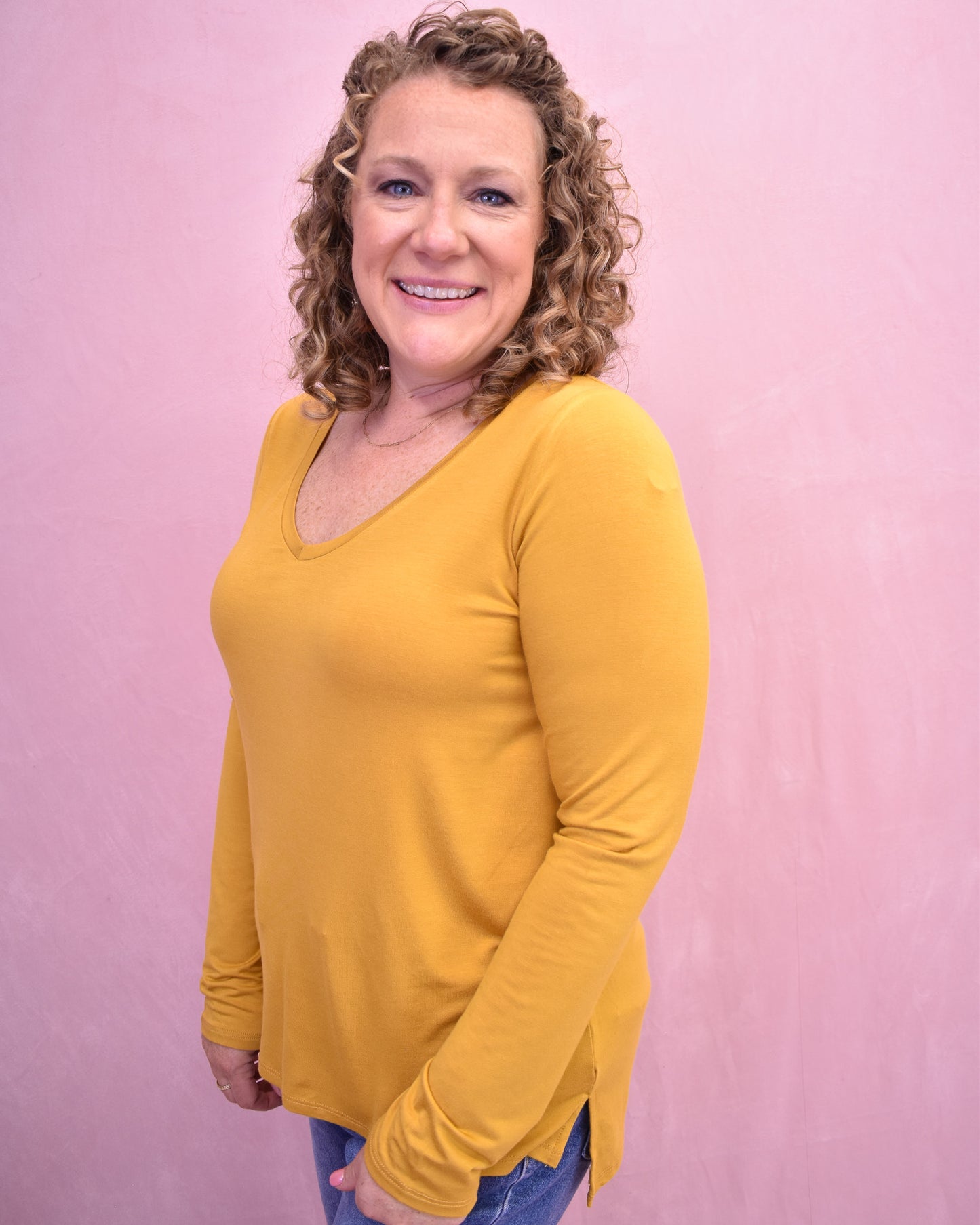 Woman wearing a yellow long-sleeve shirt against a pink background