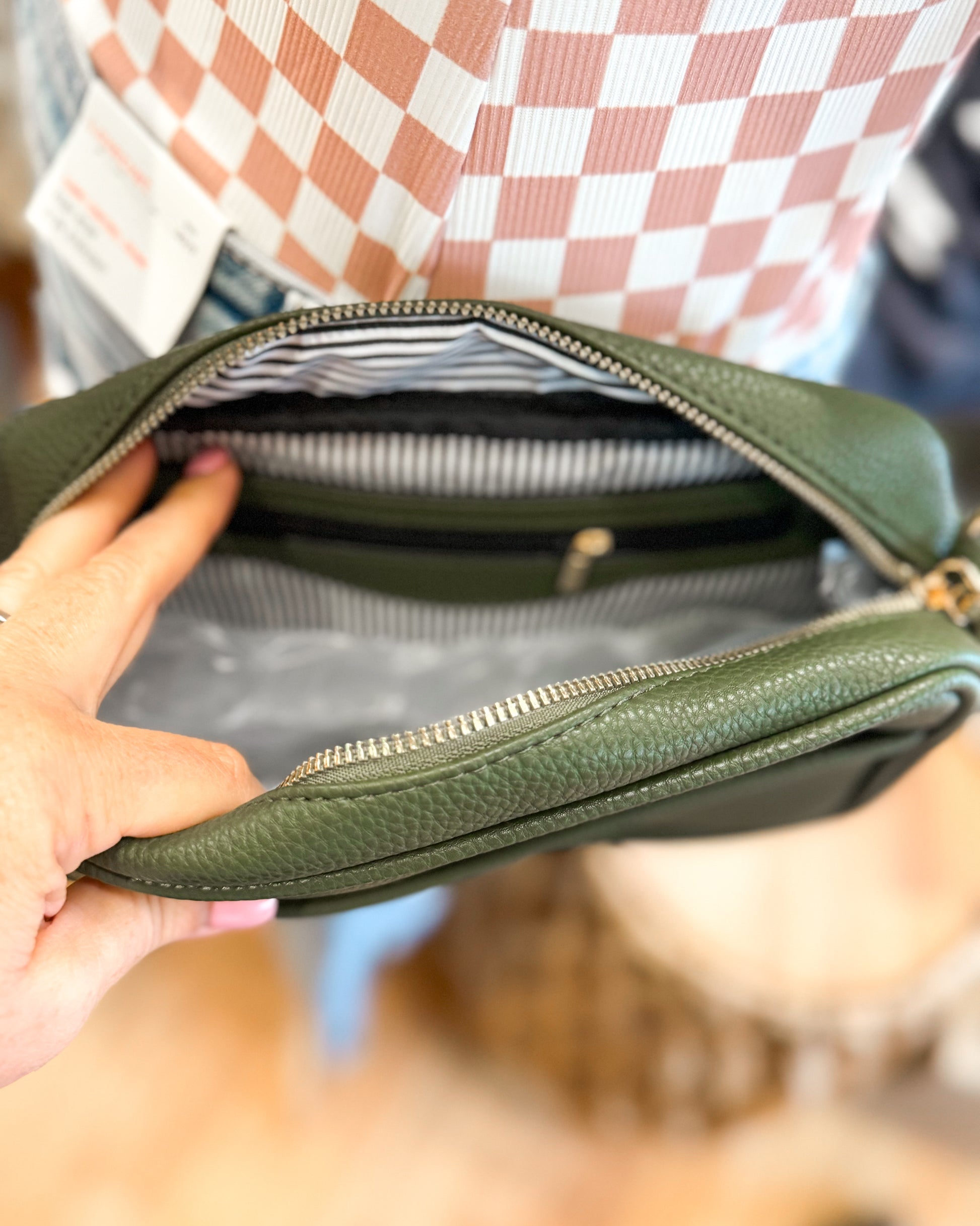 Green leather bag held by a person with a checkered shirt in the background