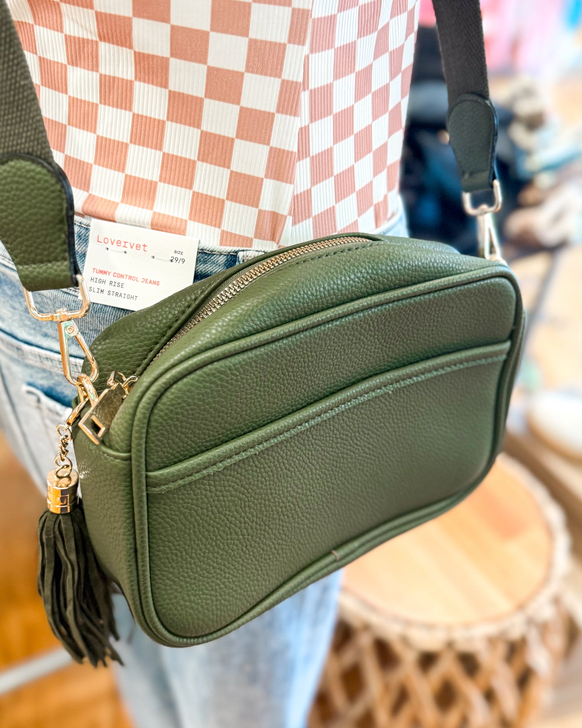 Green crossbody bag with a tassel detail worn by a person, blurred background