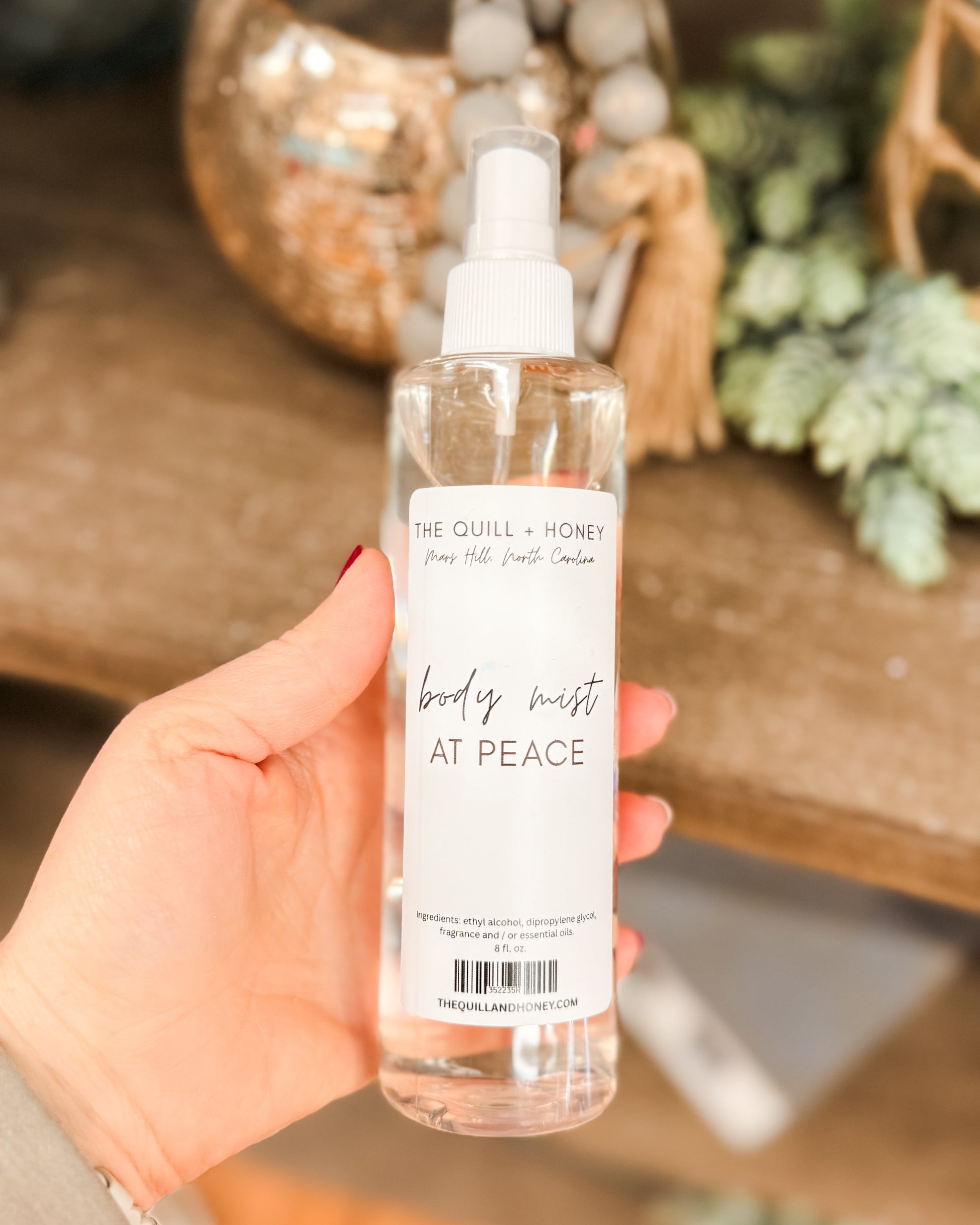 Hand holding a bottle of 'At Peace' body mist with decorative background