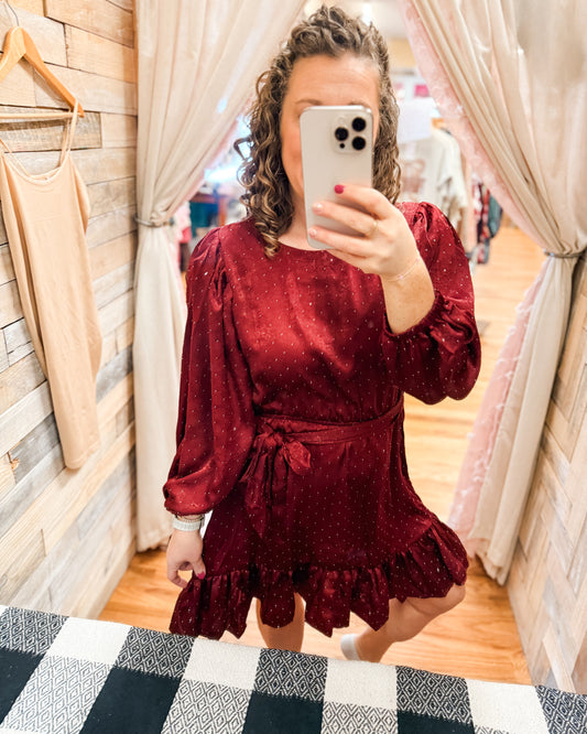 Person wearing a burgundy dress taking a mirror selfie in a store.
