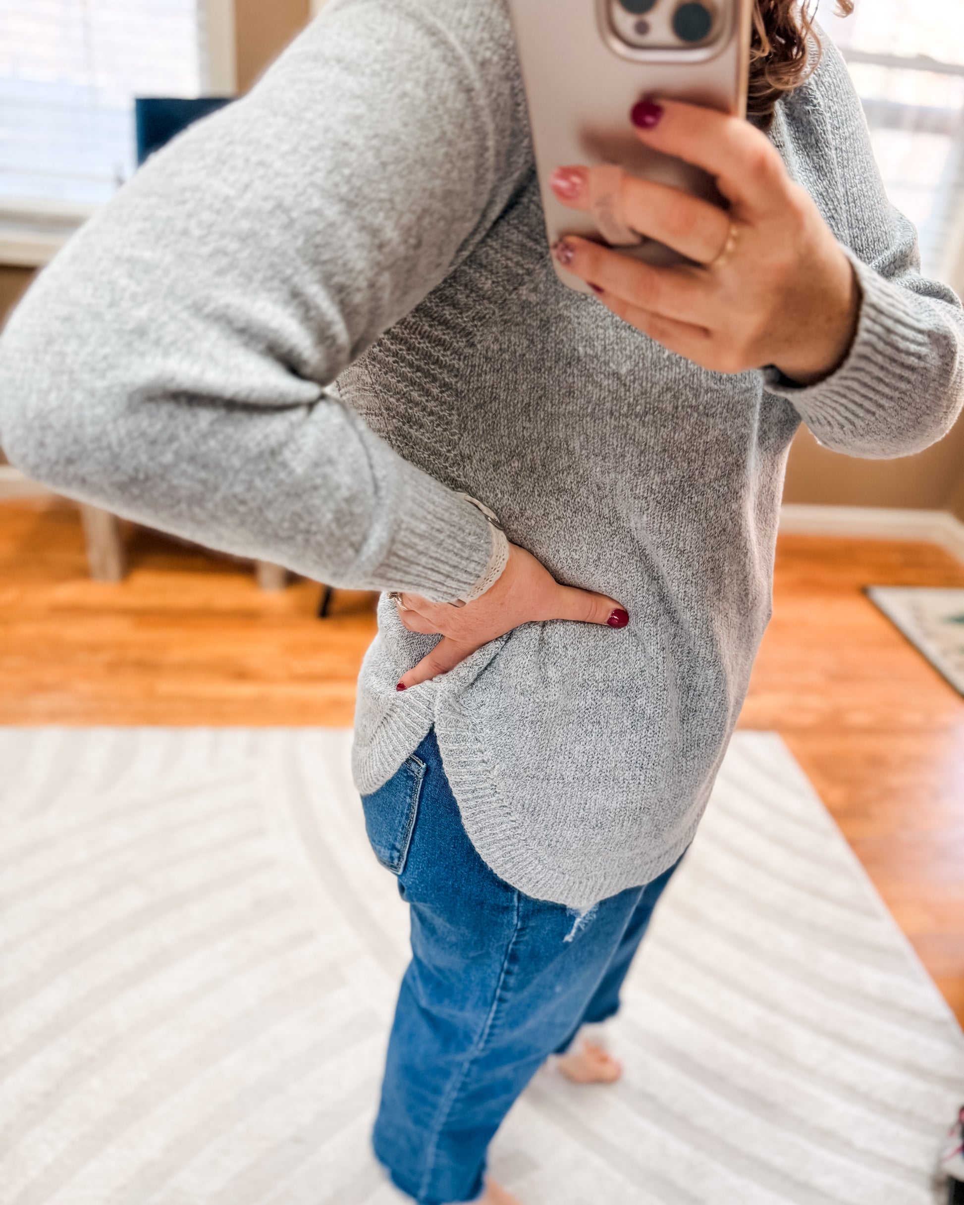 Person wearing a gray sweater and blue jeans indoors.