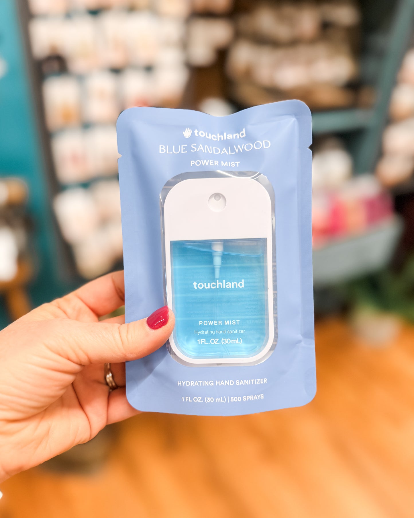 Hand holding a blue sandalwood power mist packaging with 'touchland' branding.