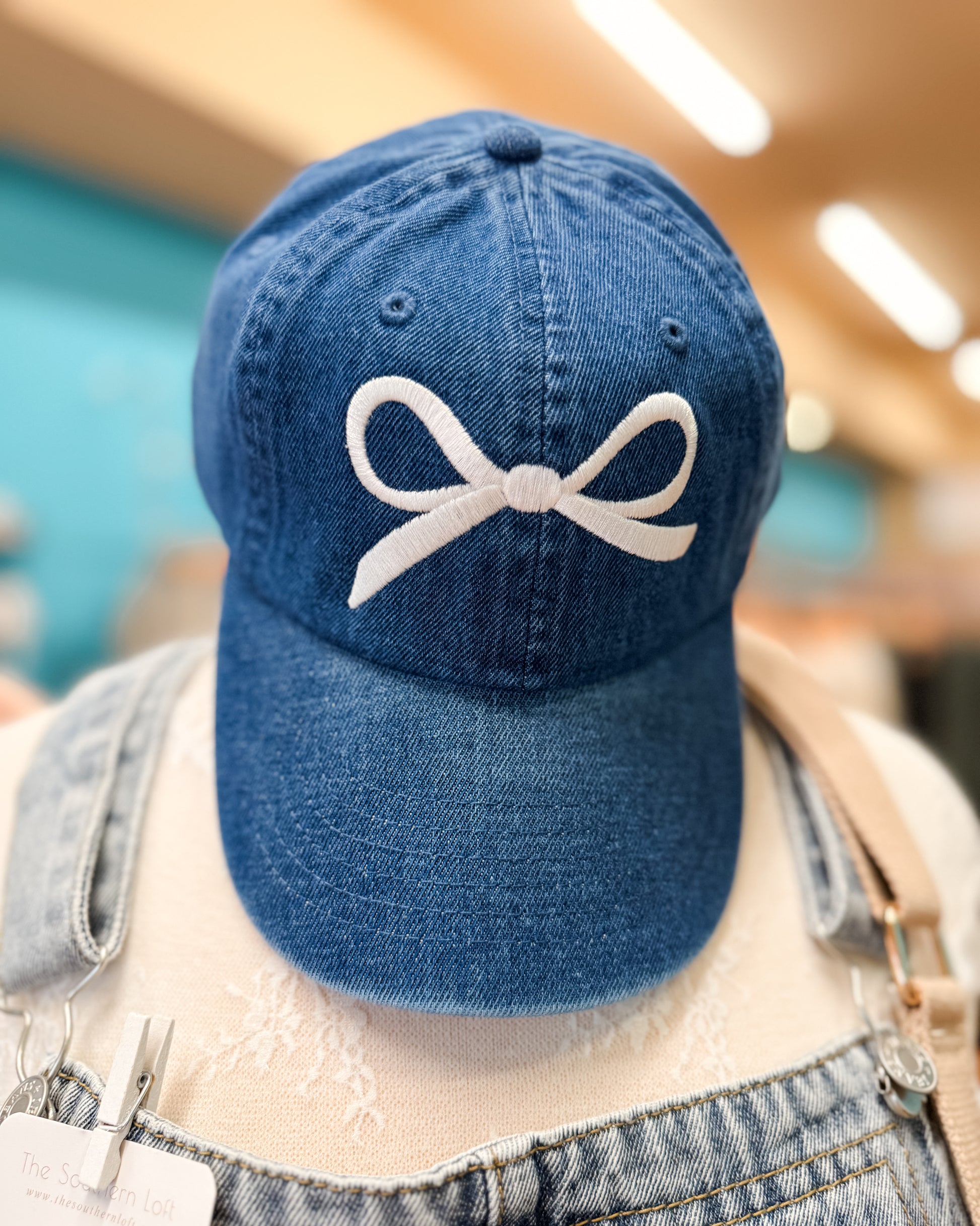 Blue denim cap with a white bow design on a mannequin head.