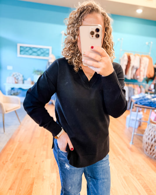 Person taking a mirror selfie wearing a black sweater and blue jeans in a store.