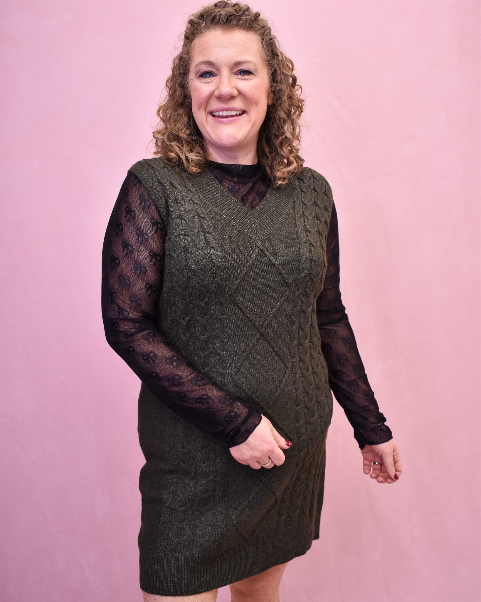 Woman wearing a green knitted dress with sheer sleeves against a pink background