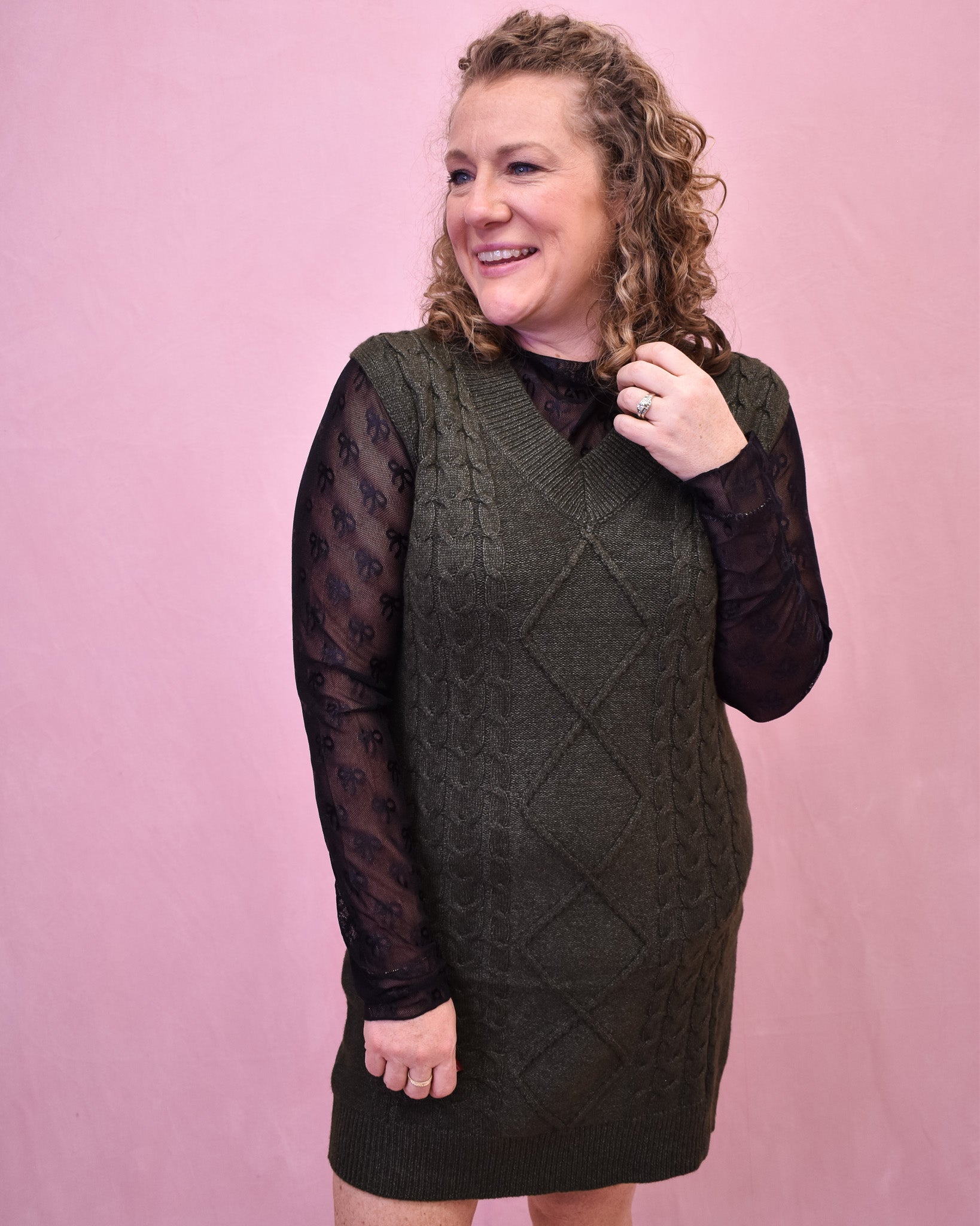 Woman wearing a green knitted dress with sheer sleeves against a pink background