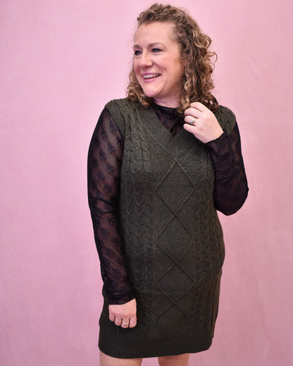 Woman wearing a green knitted dress with sheer sleeves against a pink background