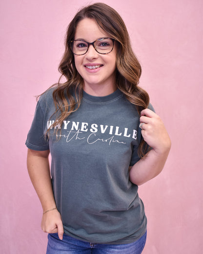 Woman wearing a blue t-shirt with 'Waynesville, North Carolina' text on a pink background