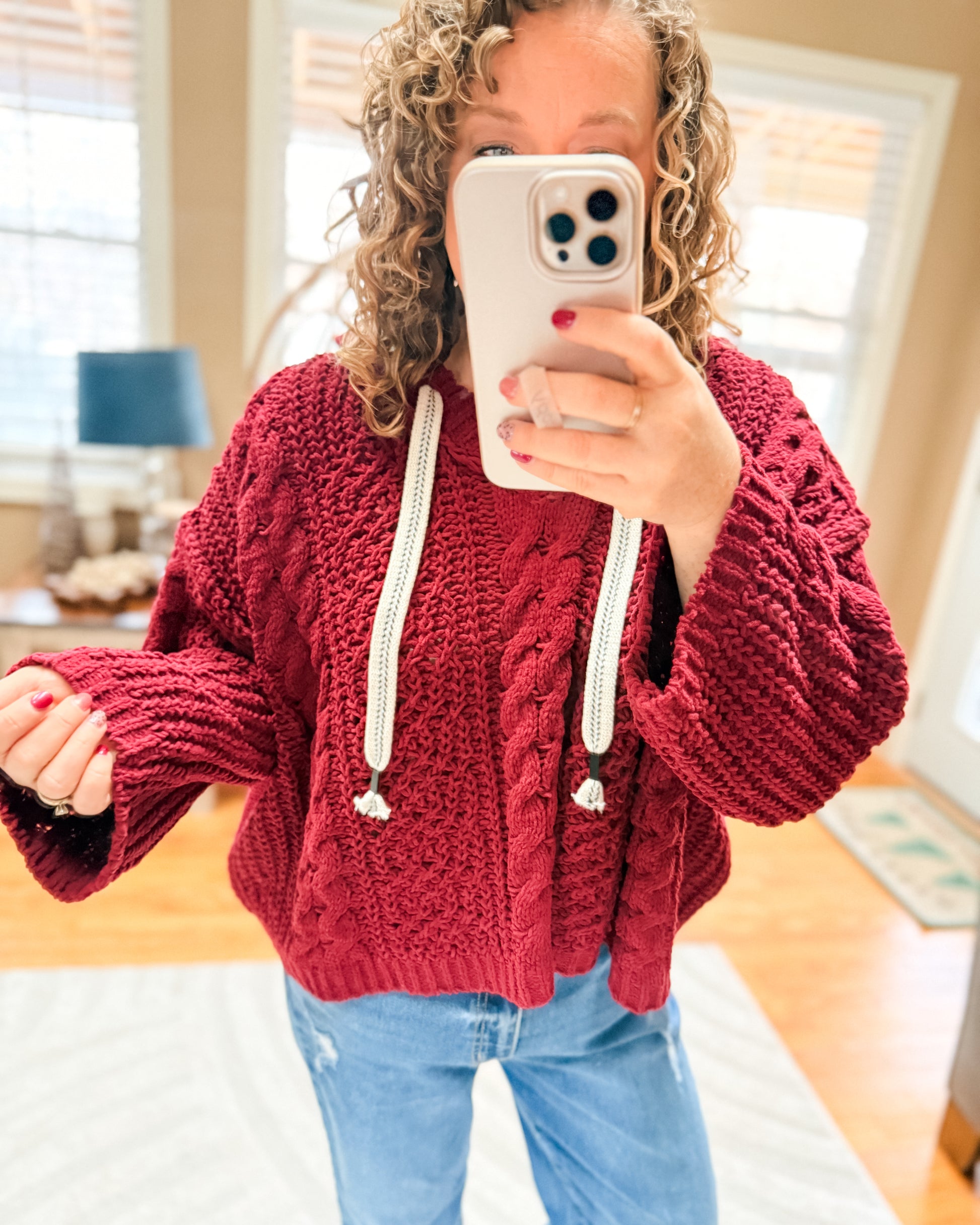 Person wearing a red knitted hoodie with white drawstrings indoors.