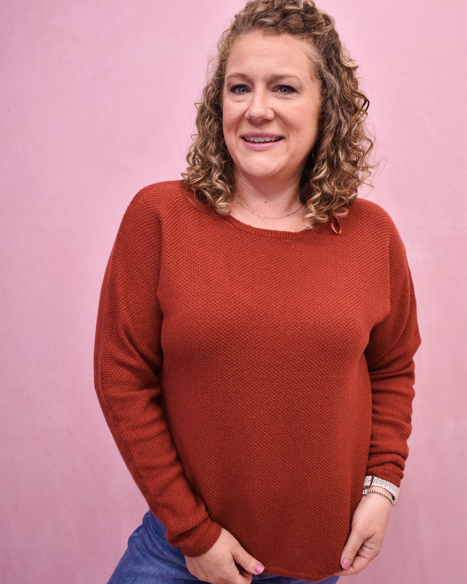 Woman wearing a rust-colored sweater against a pink background