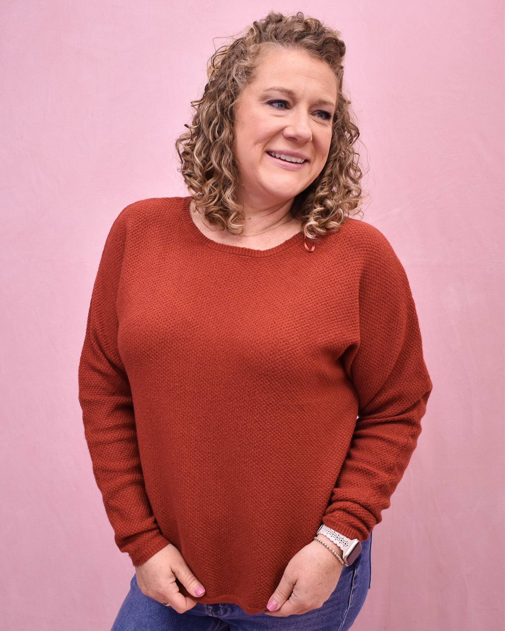 Woman wearing a rust-colored sweater against a pink background