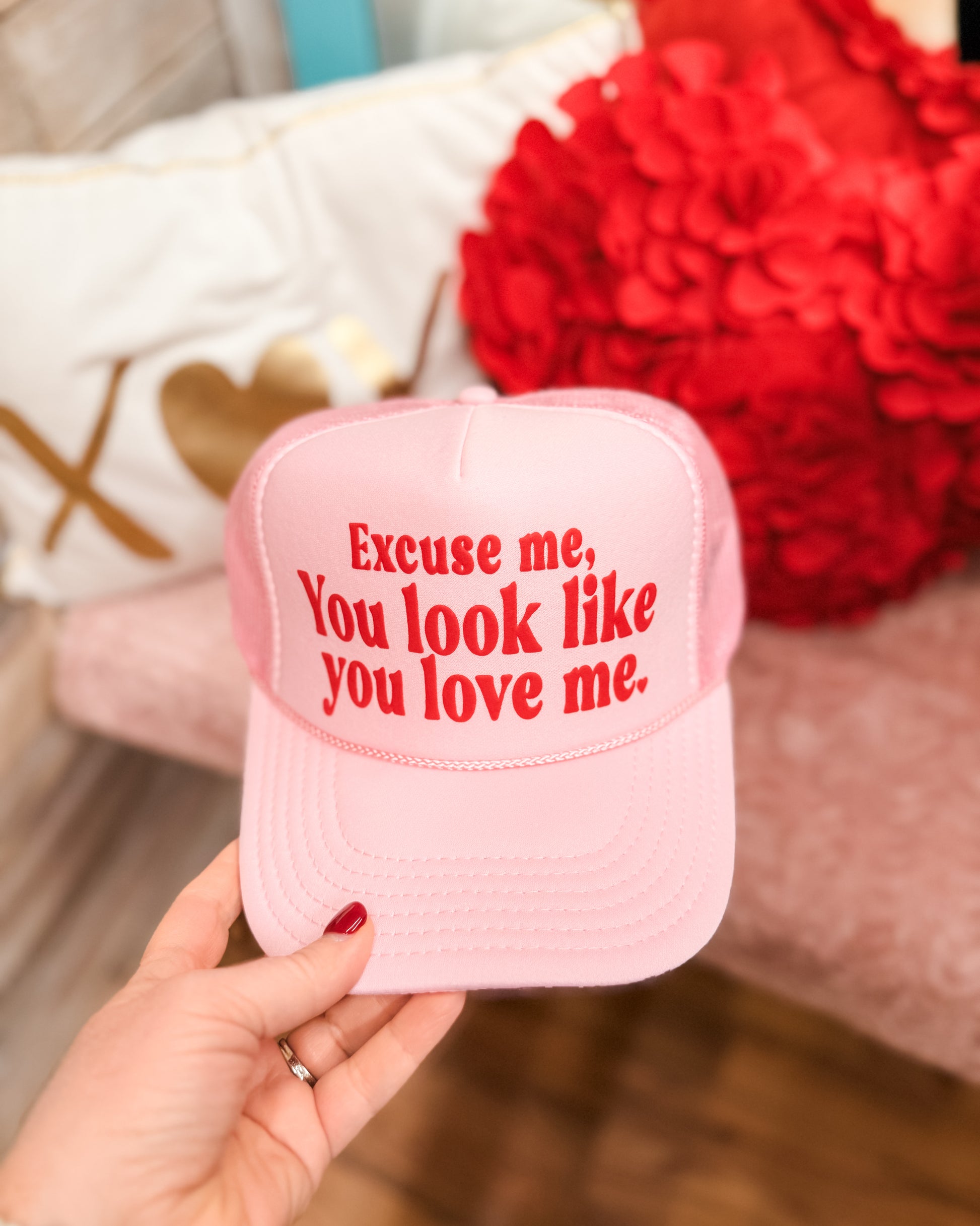 Pink cap with red text held by a hand, with a blurred background of flowers and fabric.